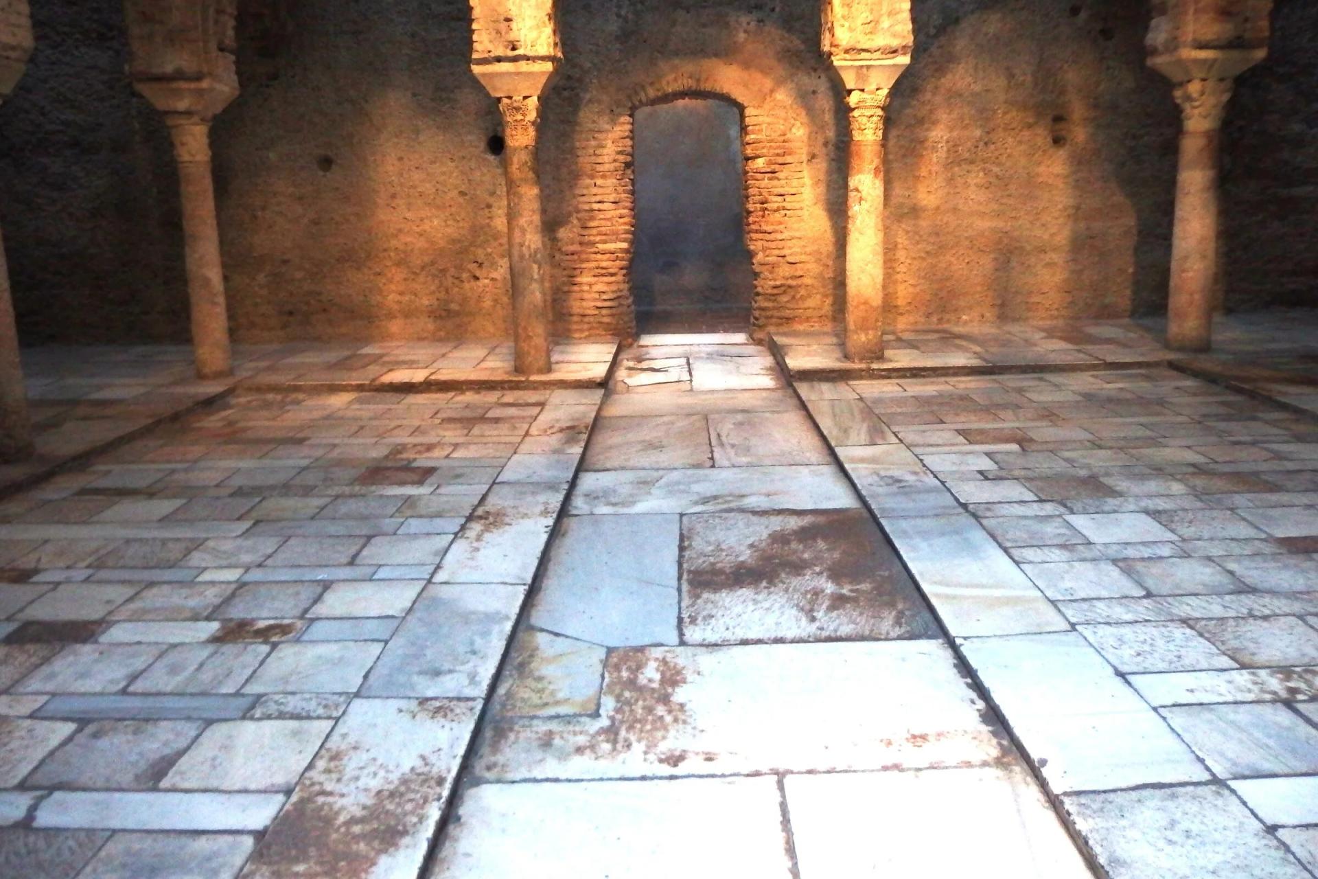 Sala de El Bañuelo con arcos de herradura de ladrillo sobre columnas y suelo de losas de mármol