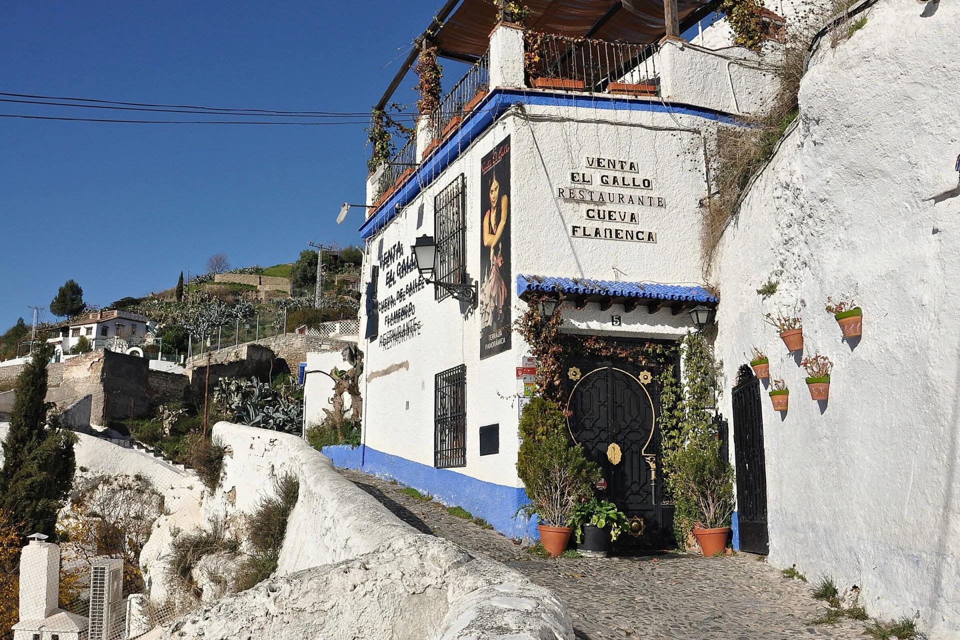 Fachada encalada de Venta El Gallo, una cueva flamenca del Sacromonte, con su rótulo y macetas en la pared