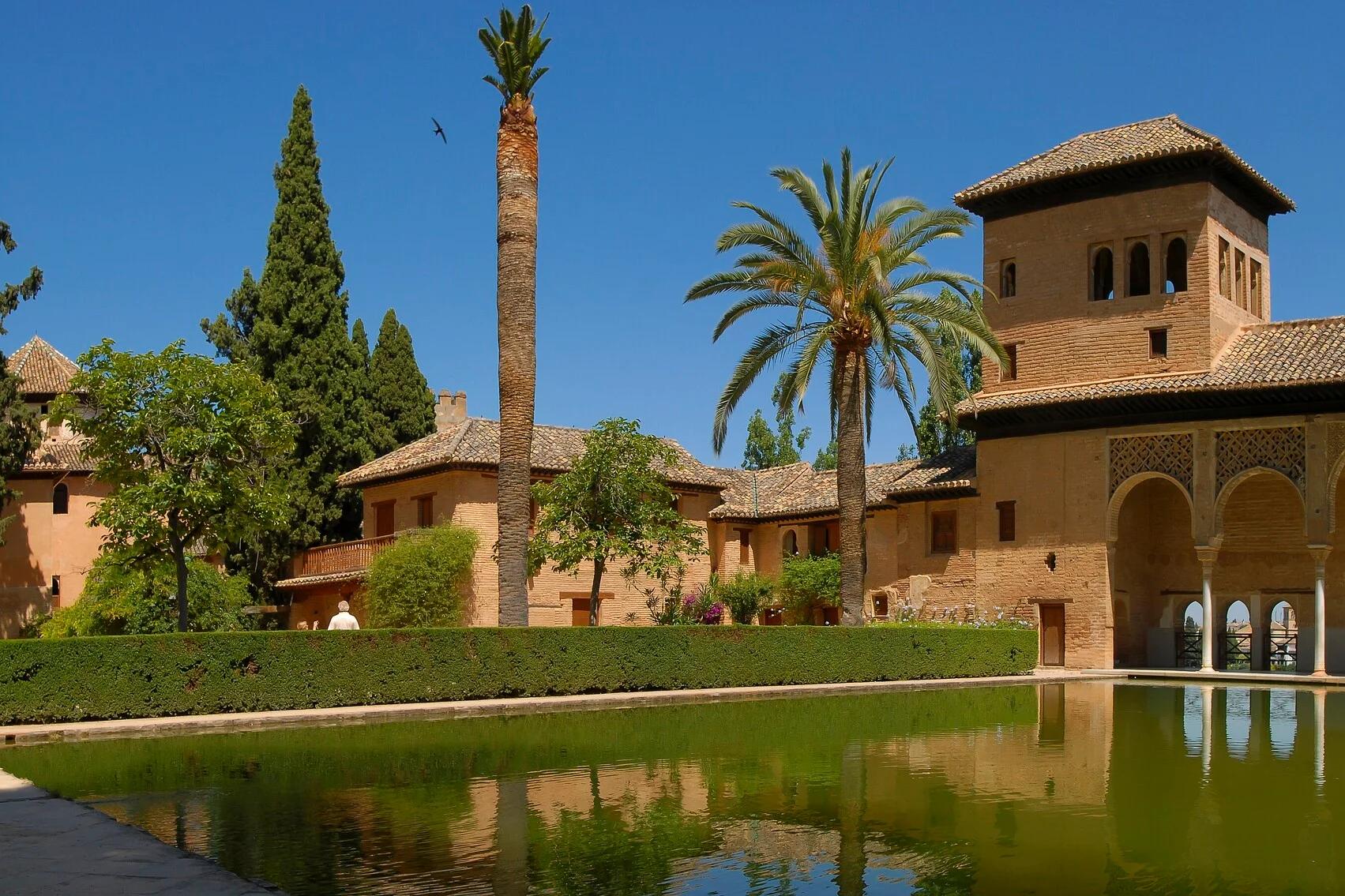 El pórtico del Partal con su torre, reflejado en el estanque entre palmeras y cipreses