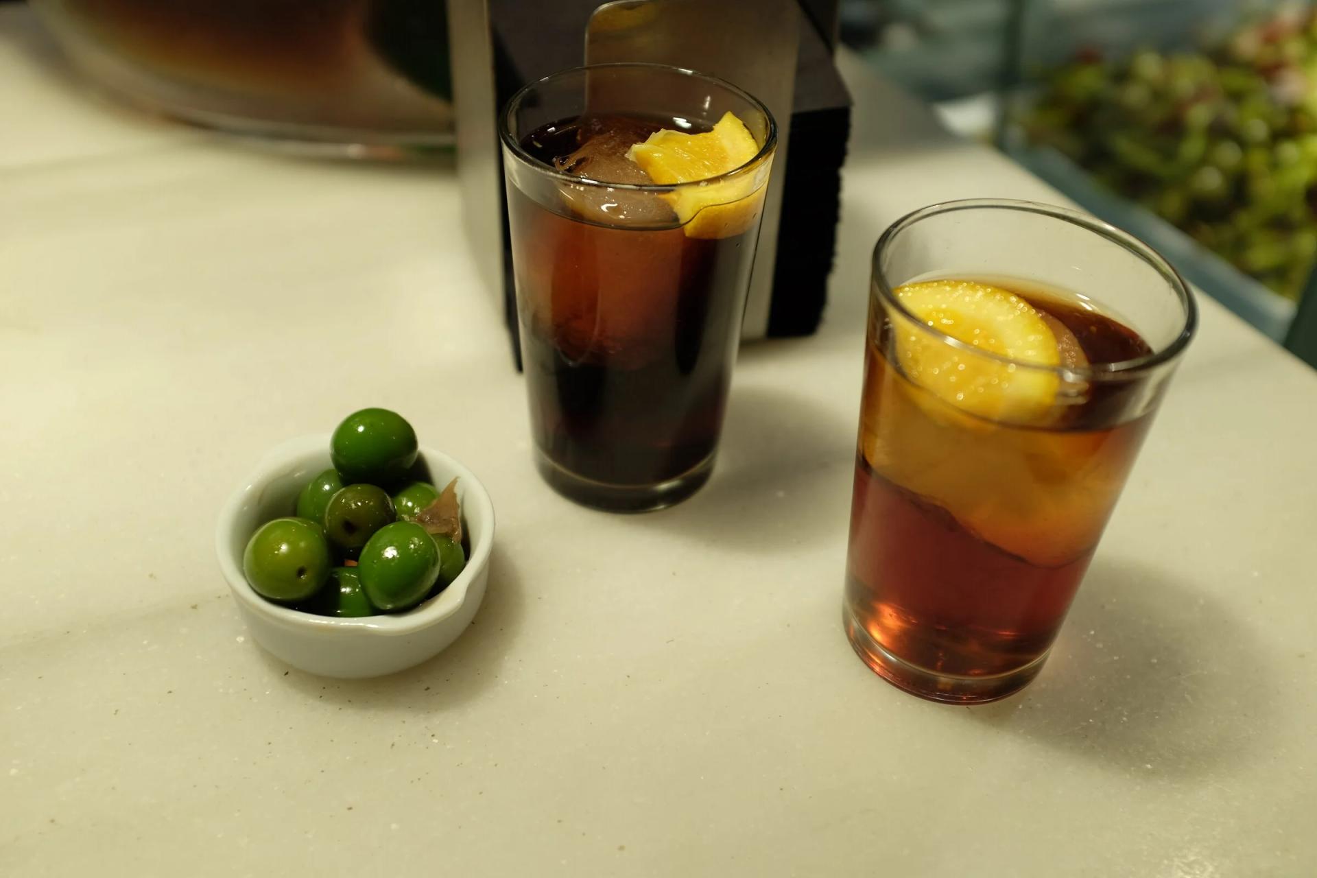 Dos vasos de vermut de grifo con hielo y limón junto a un cuenco de aceitunas, la bebida que se pide en Bodegas Castañeda