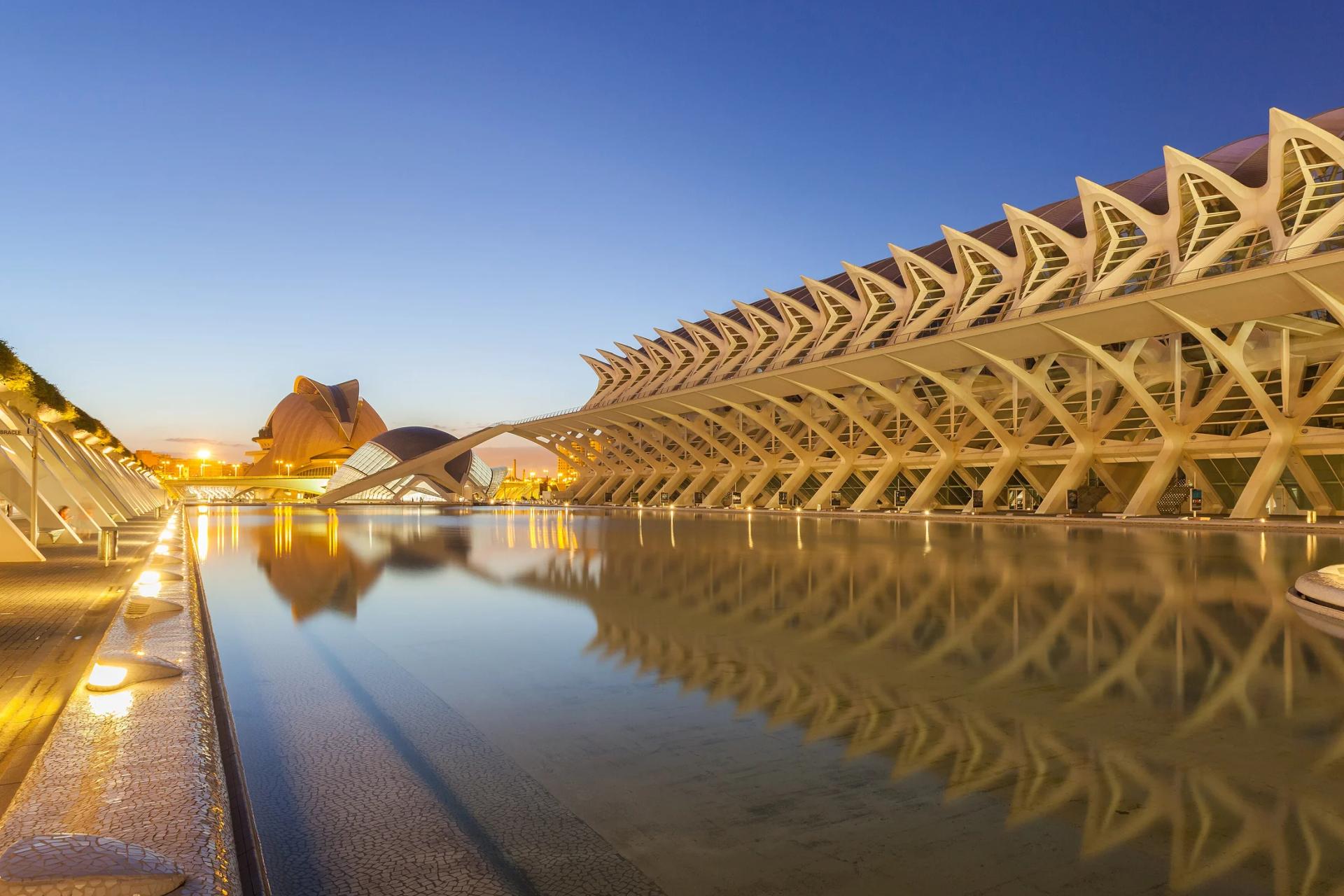 El Museo de las Ciencias iluminado en la hora azul, con el Hemisfèric al fondo, reflejados en el agua