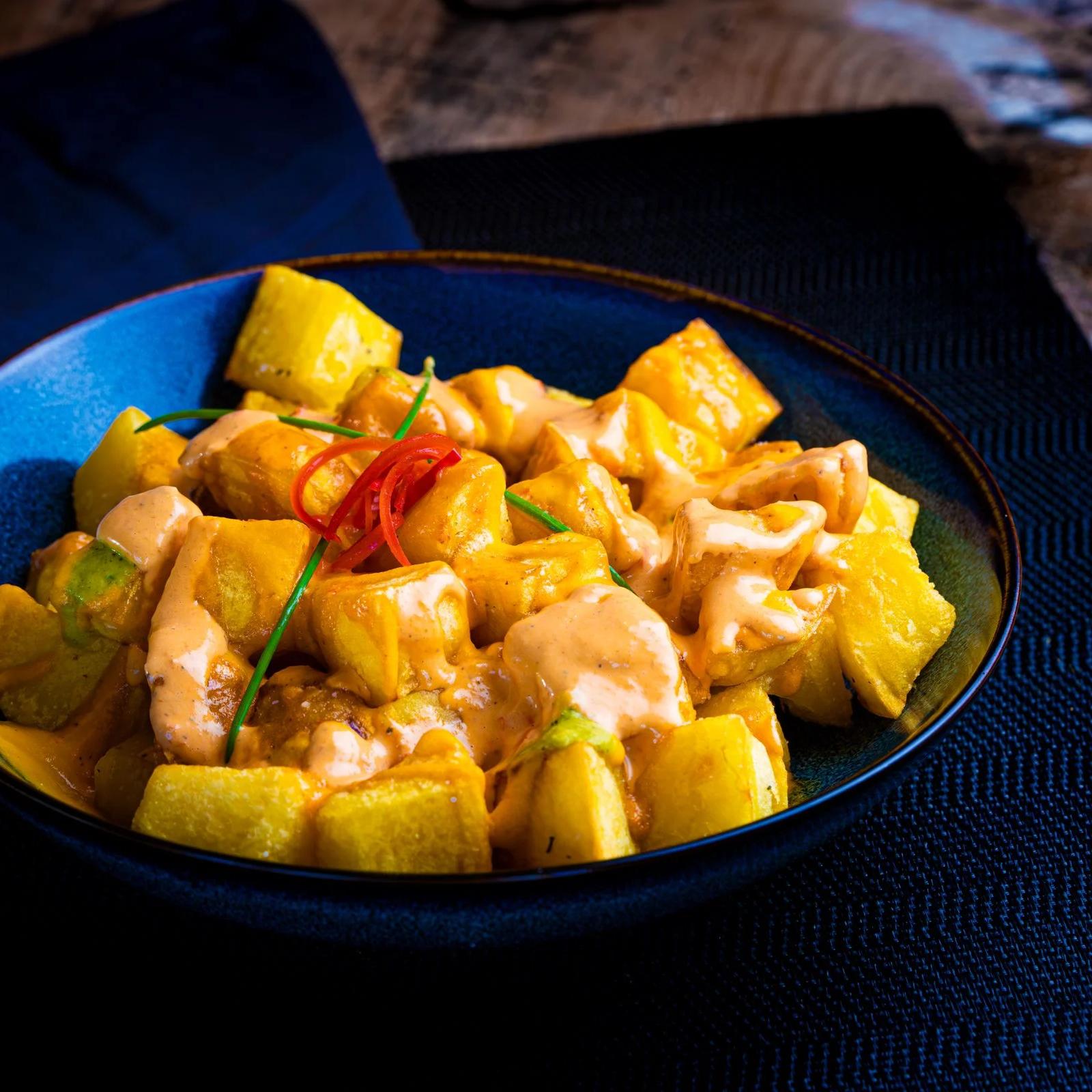 Ración de patatas bravas con salsa en un cuenco azul