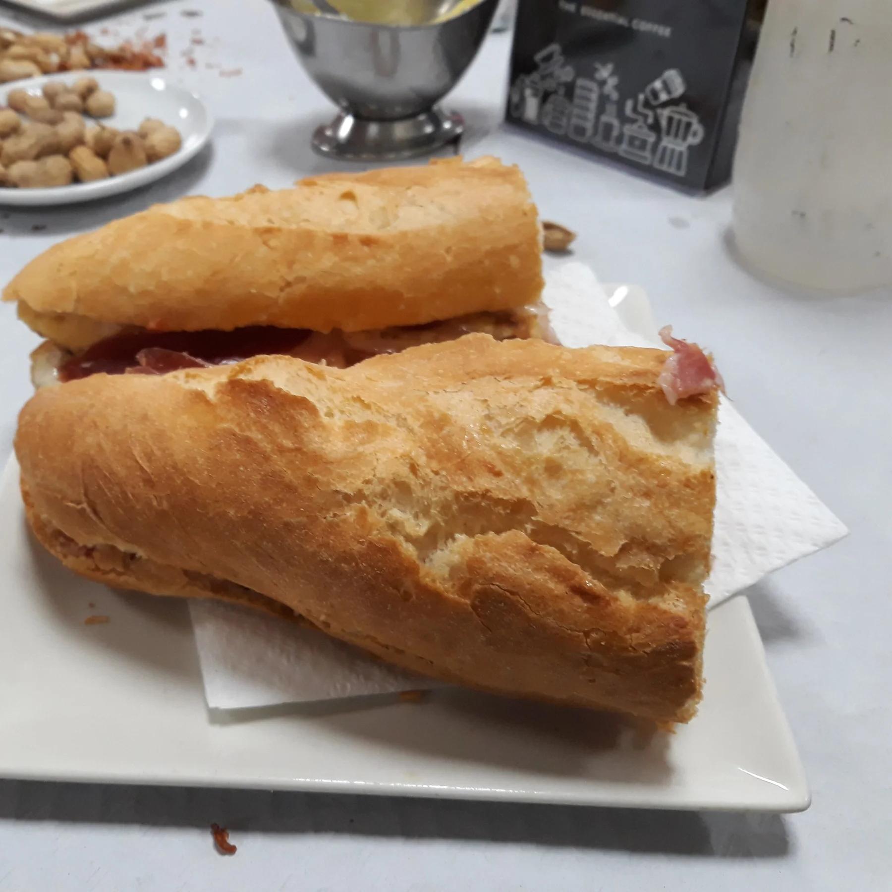Un bocadillo de almuerzo valenciano en un plato, con cacahuetes en la mesa