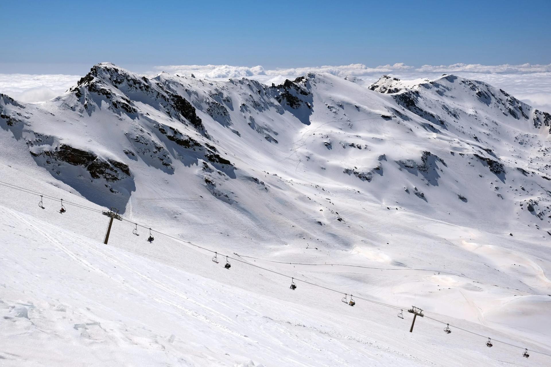Cumbres nevadas de Sierra Nevada sobre un mar de nubes, con un telesilla en la zona de Laguna de las Yeguas