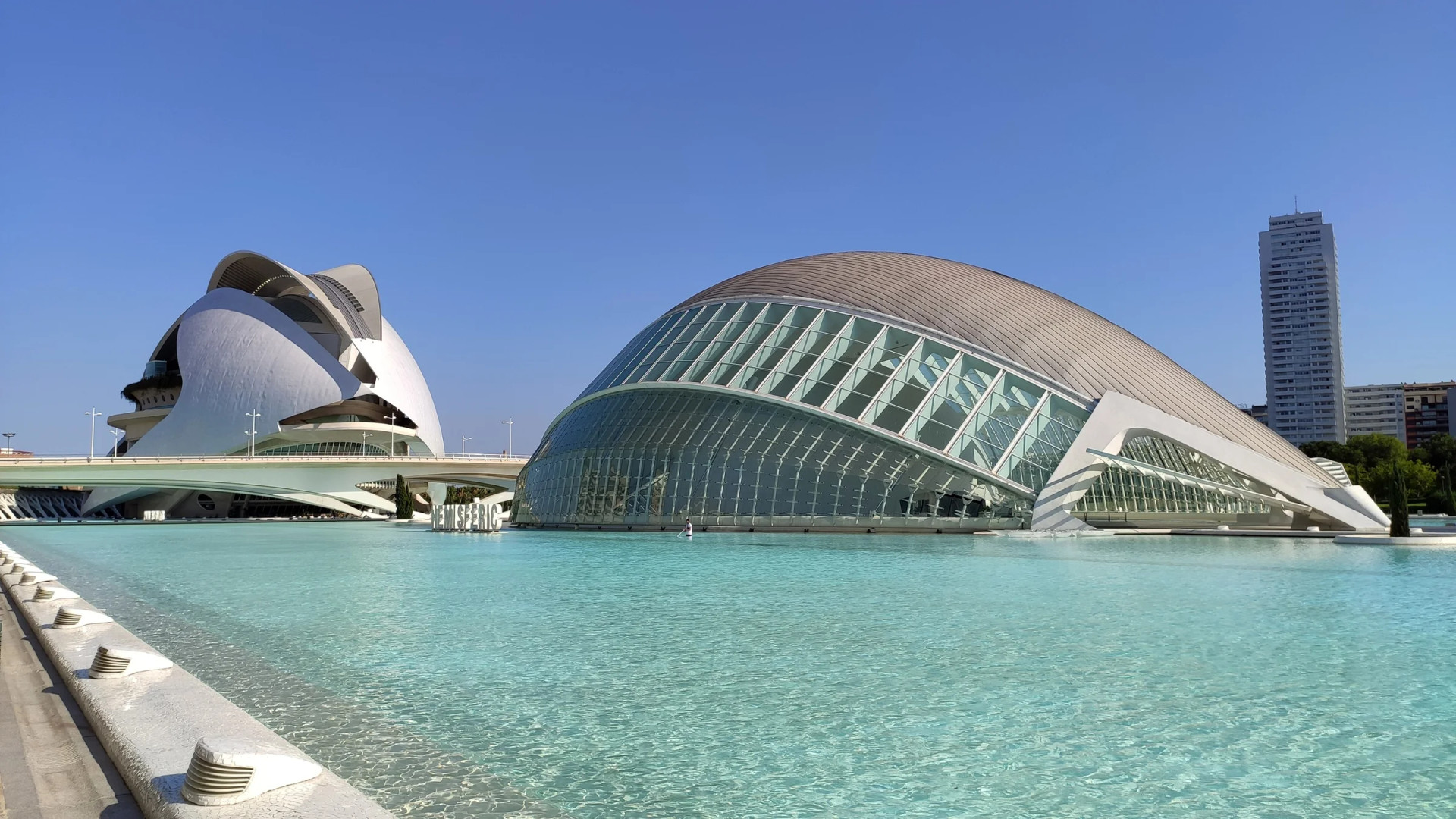 El Palau de les Arts y el Hemisfèric junto a la lámina de agua de la Ciudad de las Artes, bajo un cielo azul