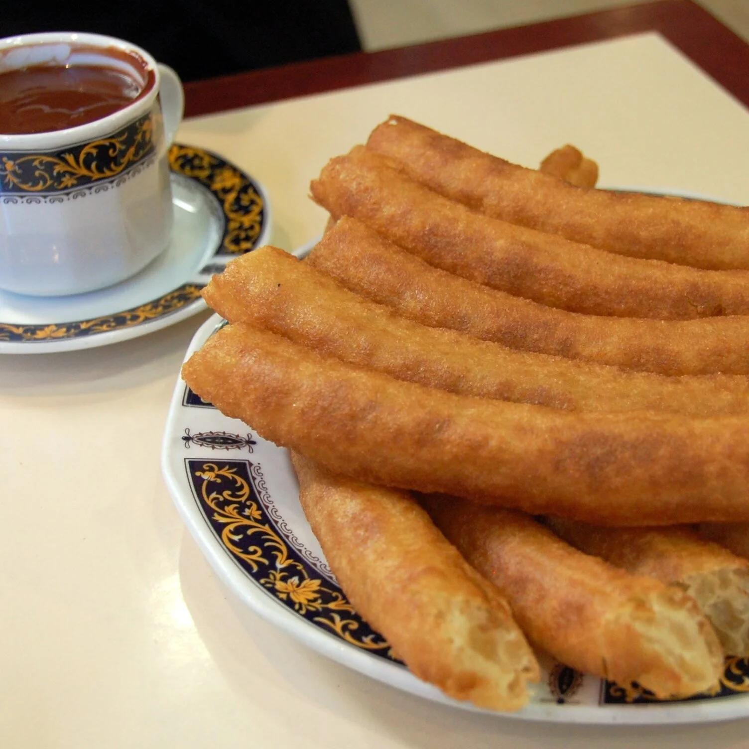 Plato de porras junto a una taza de chocolate caliente en una cafetería de Granada