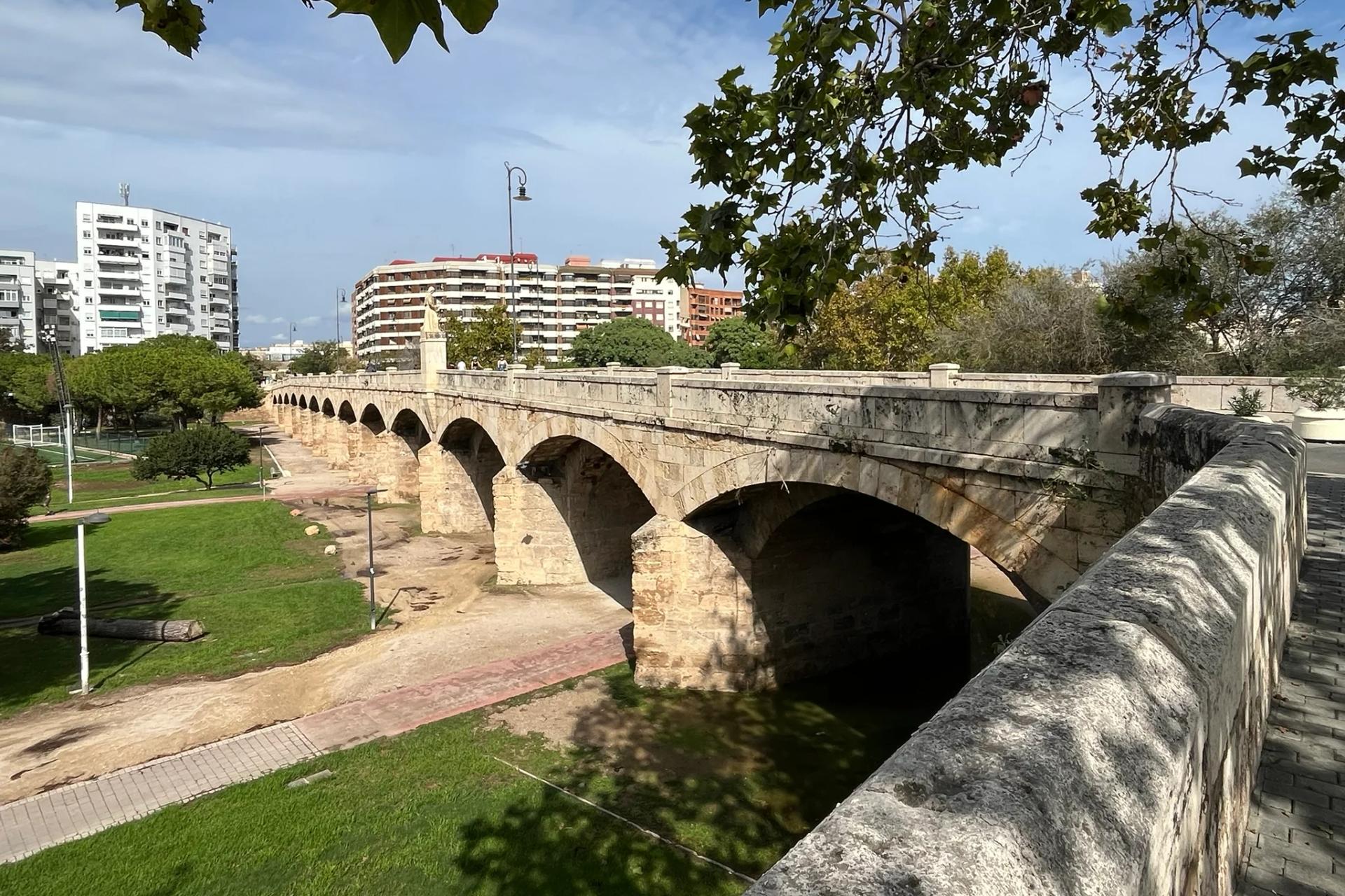 El puente de San José, de piedra, sobre el césped y los árboles del Jardín del Turia