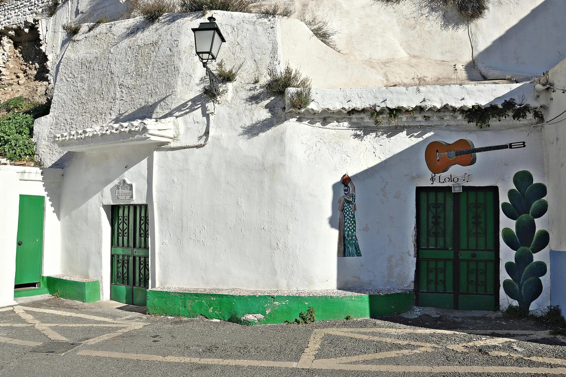 Fachada encalada de la Cueva de la Zíngara en el Sacromonte, con puertas verdes y una guitarra pintada