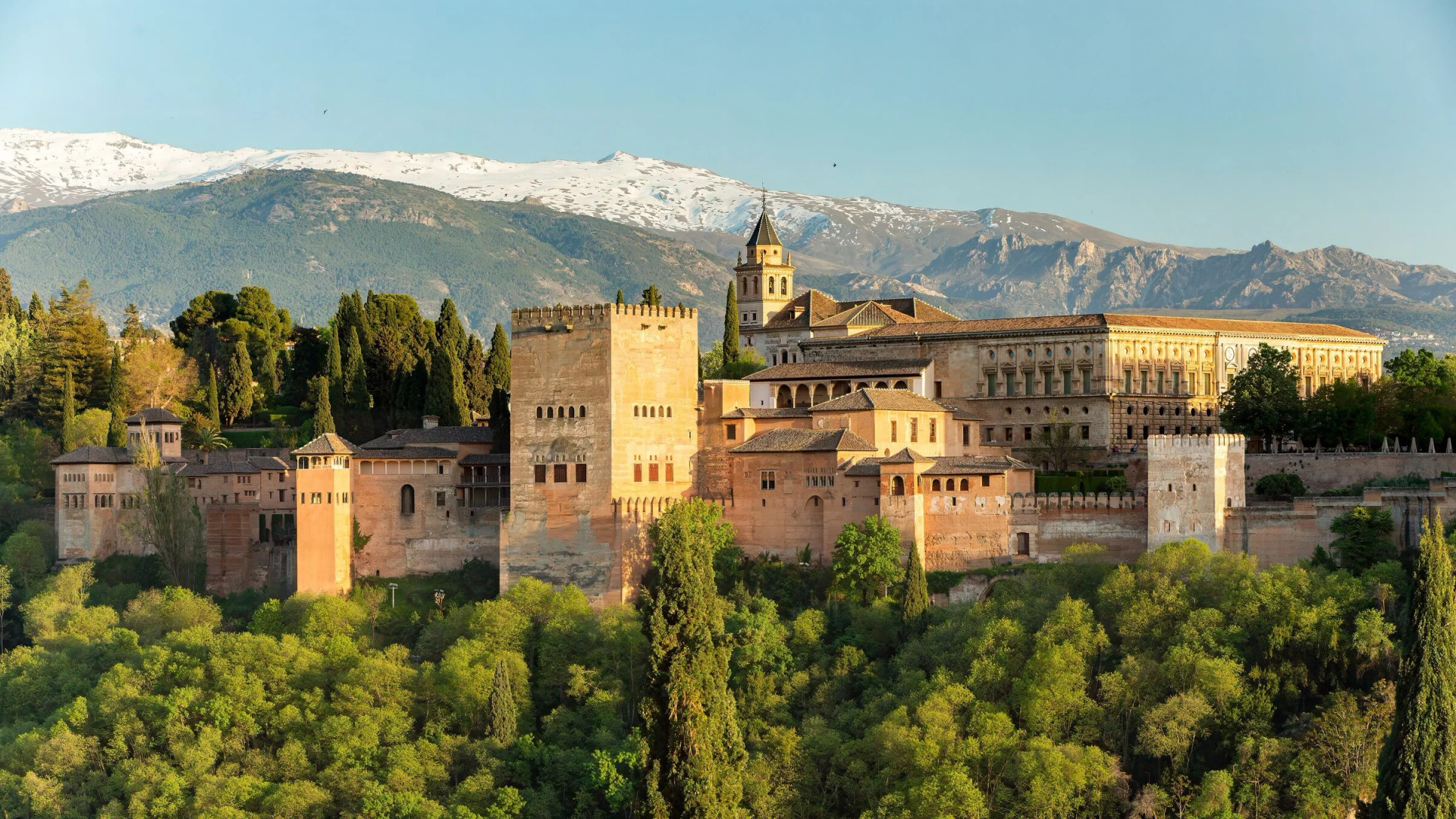 La Alhambra al atardecer desde el mirador de San Nicolás, con el Palacio de Carlos V y las cumbres nevadas de Sierra Nevada al fondo