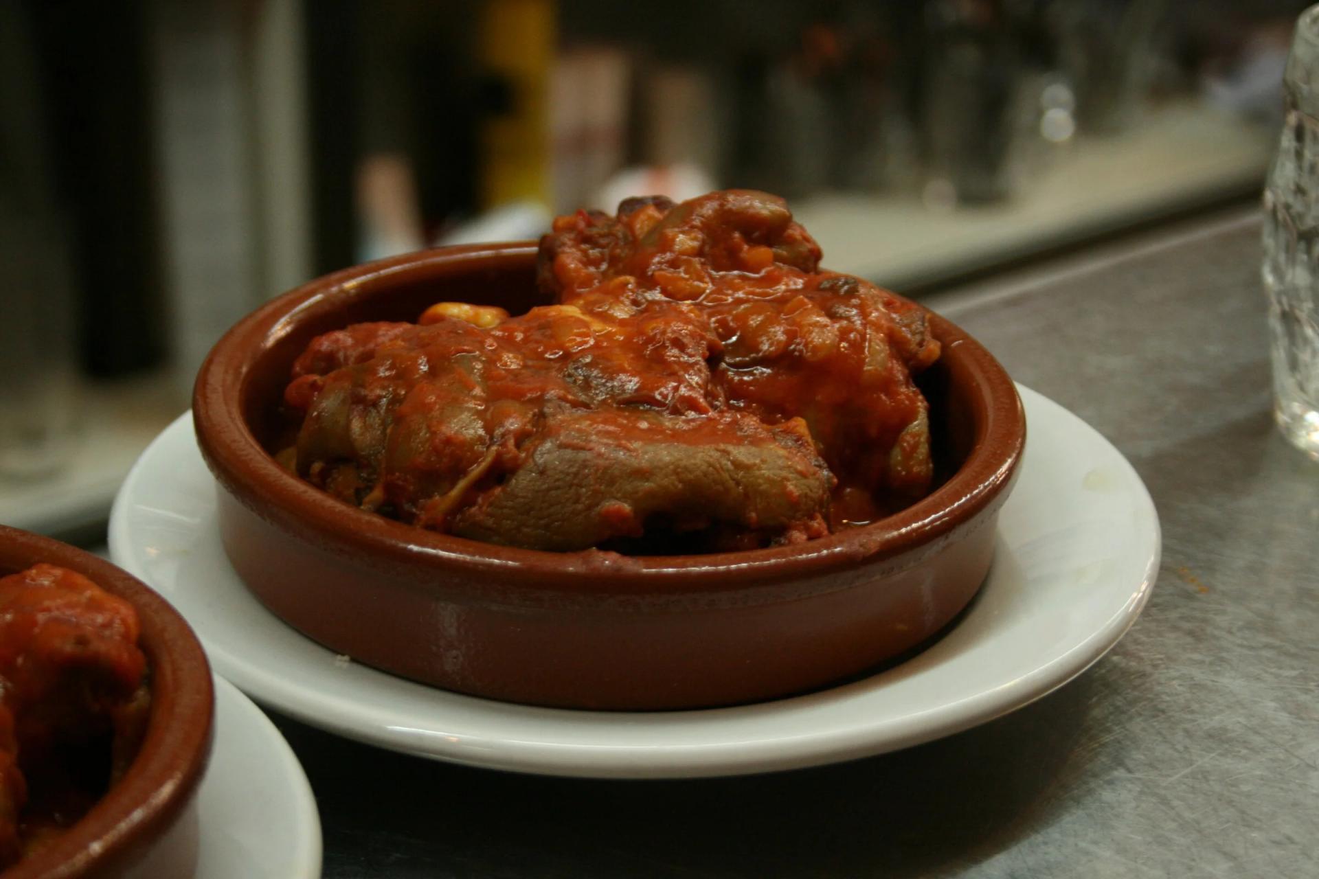 Cazuelita de manitas de cerdo en salsa de tomate sobre una barra, el plato estrella de La Sitarilla